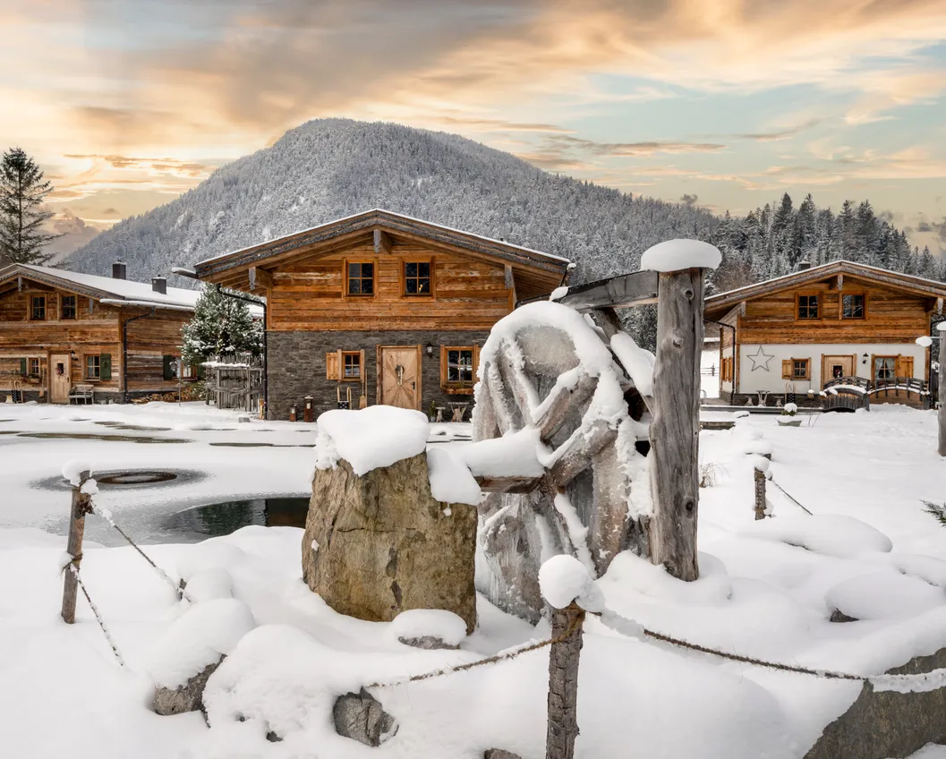 Tyrolean village in snow at sunset with wooden houses and stone fountain in Biberwier
