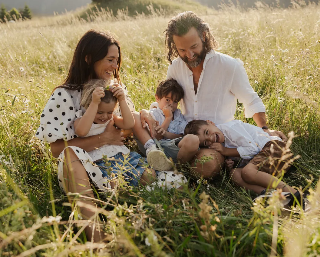 Family of five laughing and cuddling happily in the tall summer grass at LaPosch