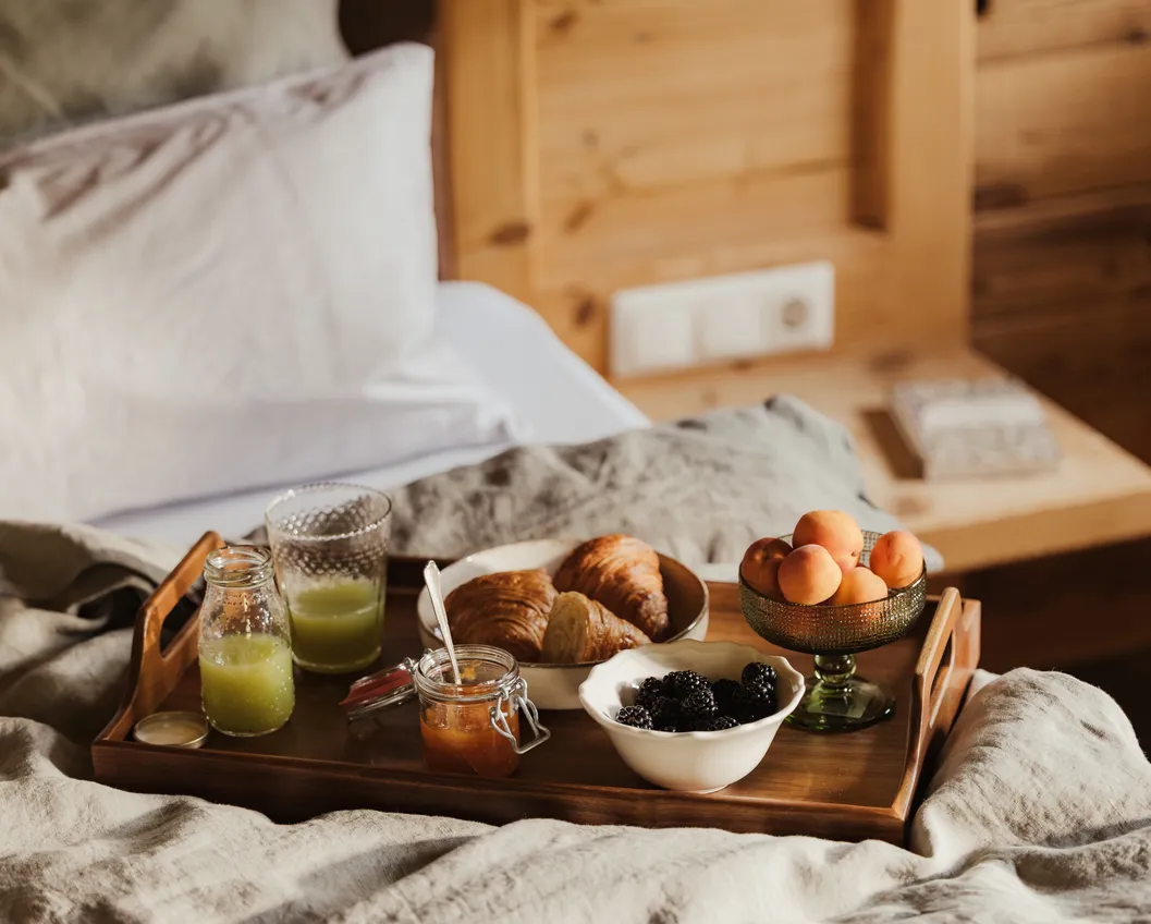 Rustic breakfast tray on a wooden bed with croissant, berries, apricots and green juice