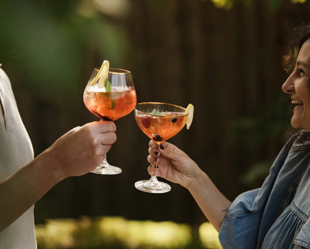 Two women laughing and clinking elegant cocktail glasses outdoors