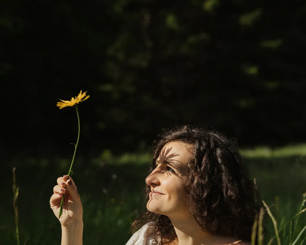 Smiling woman in a summer dress holding a yellow wildflower in the alpine meadow