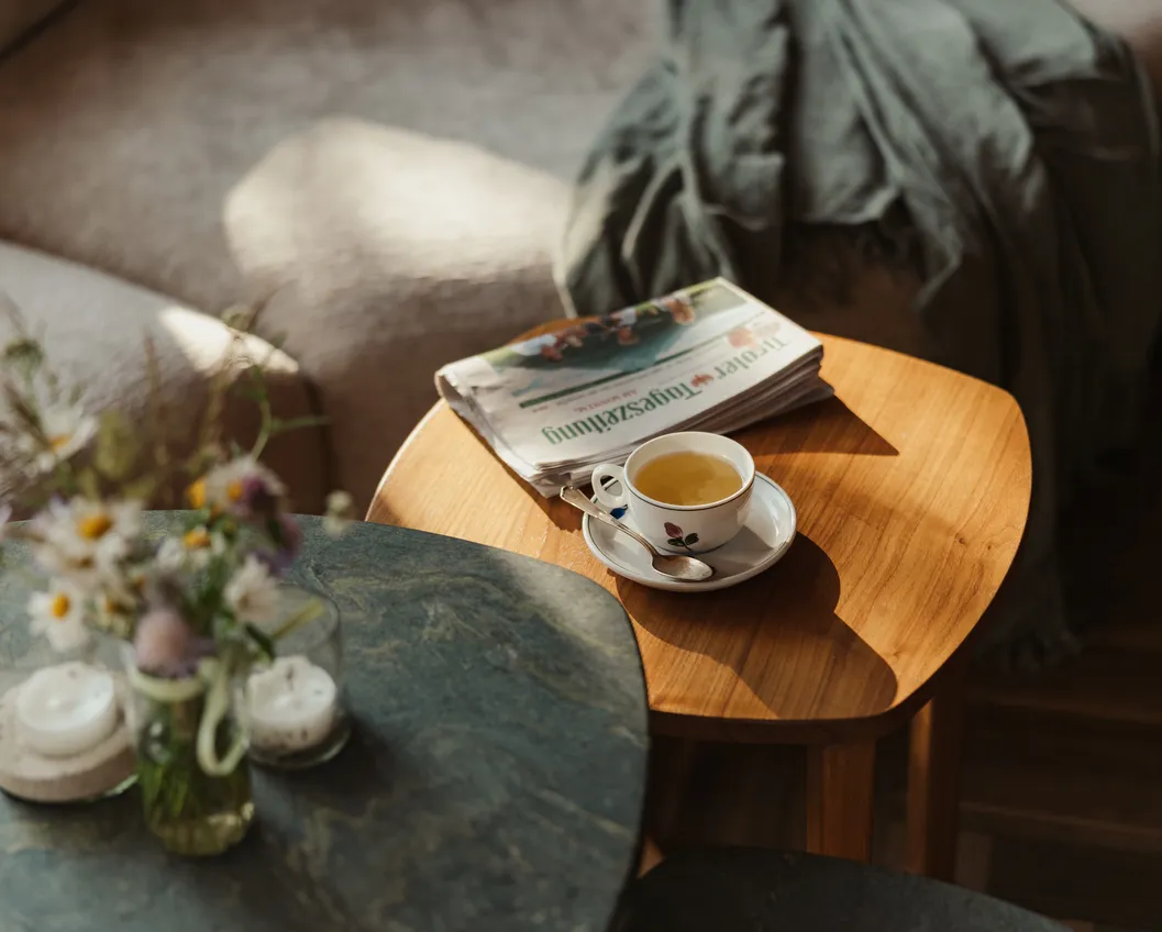 Tea cup and newspaper on a wooden side table with wildflowers, candles and a blanket