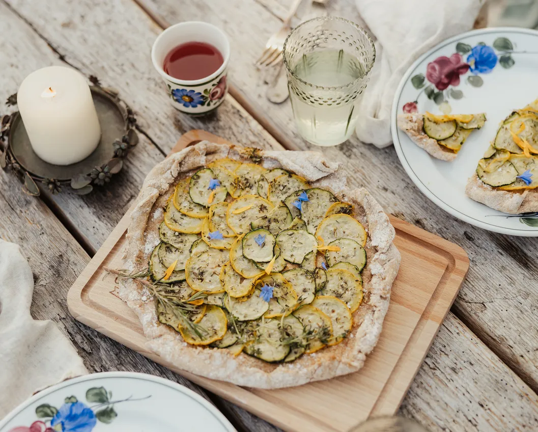 Top view of a home-made courgette galette on a wooden board with candle and drinks