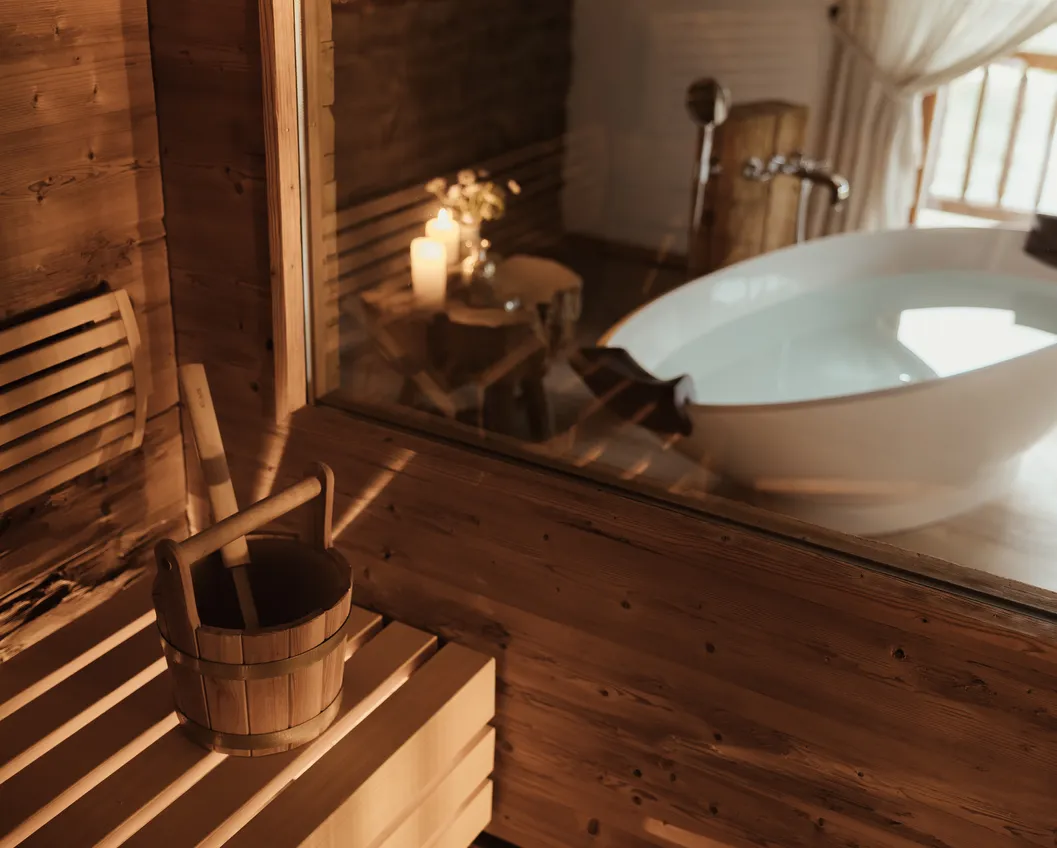 Chalet spa with wooden sauna, water bucket and freestanding white soaking tub by candlelight