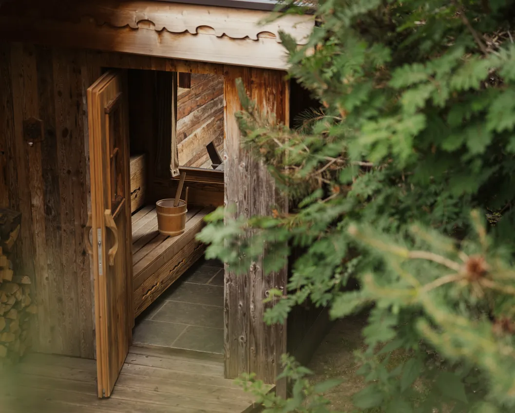 Rustic open sauna cabin of weathered wood with a water bucket and ladle
