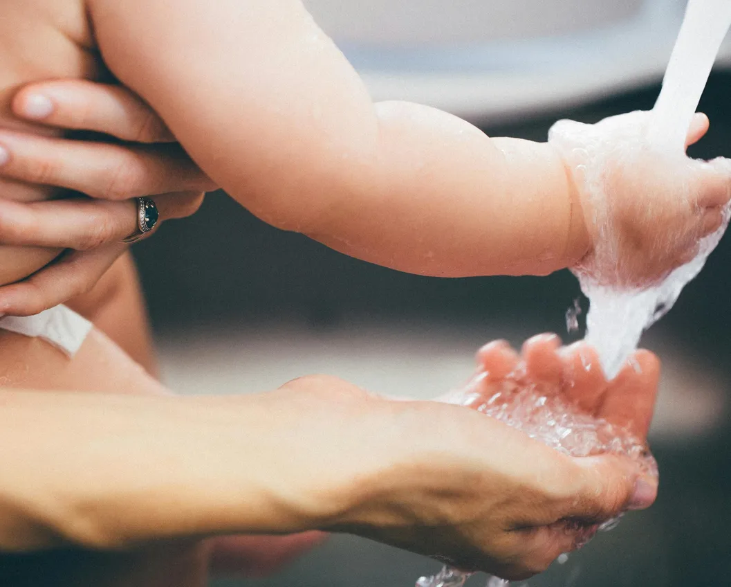 Caring hands washing a baby's hand under running water in gentle soft light