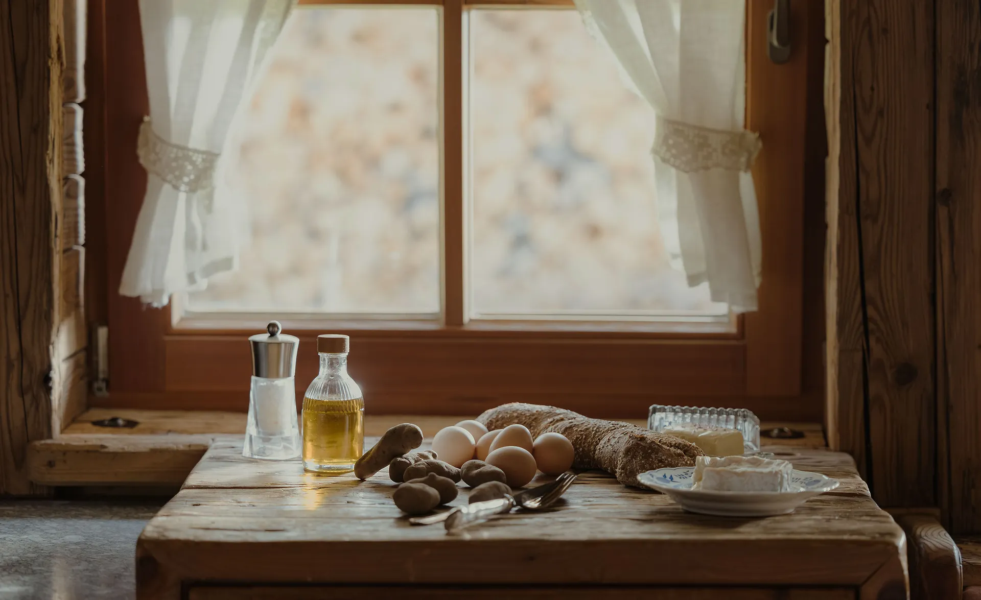 Rustikales Landhaus-Stillleben mit Eiern, Kartoffeln, Brot, Öl und Butter am Chalet-Fenster
