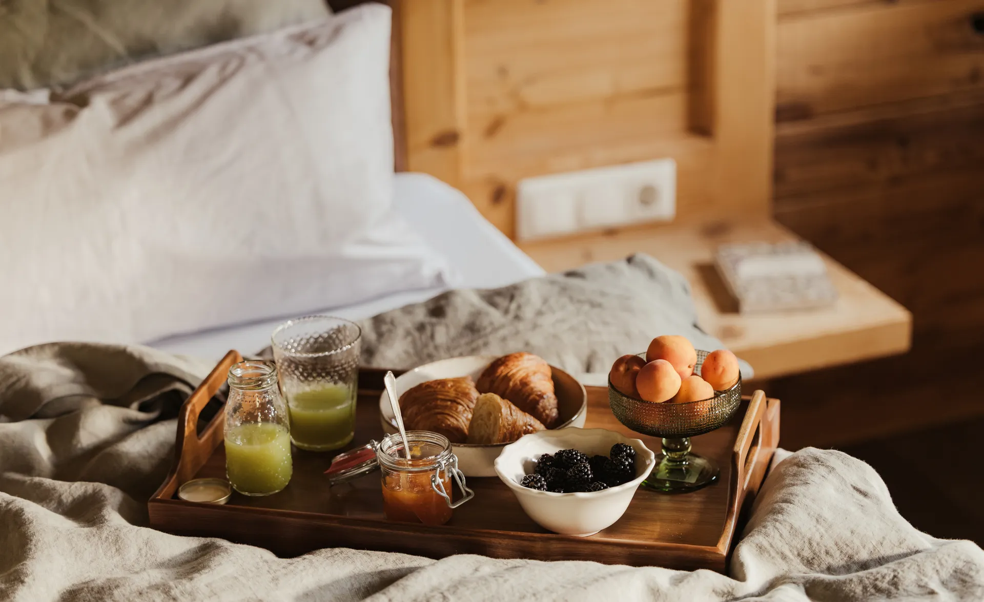 Rustikales Frühstückstablett auf Holzbett mit Croissant, Beeren, Marillen und Grünsaft