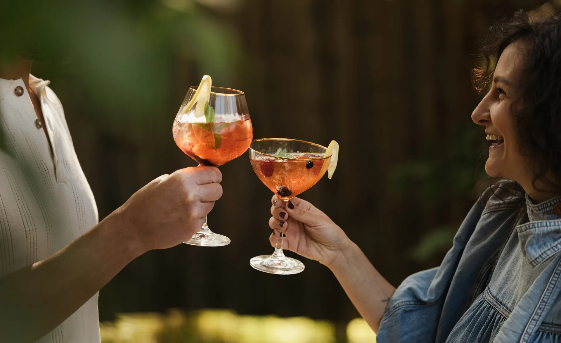 Zwei Frauen stoßen lachend mit eleganten Cocktailgläsern im Freien an