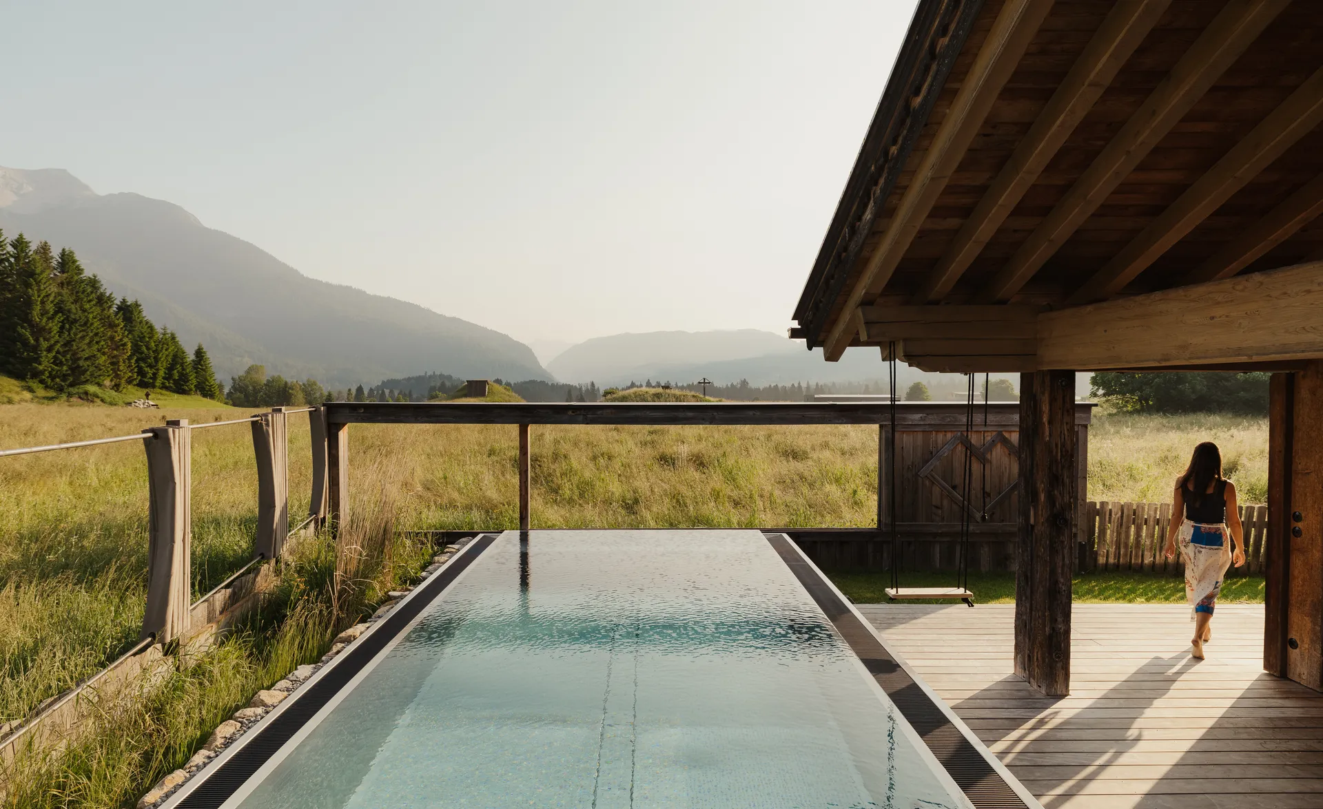 Frau geht am langen Infinity-Pool am LaPosch Chalet mit Alpenpanorama entlang