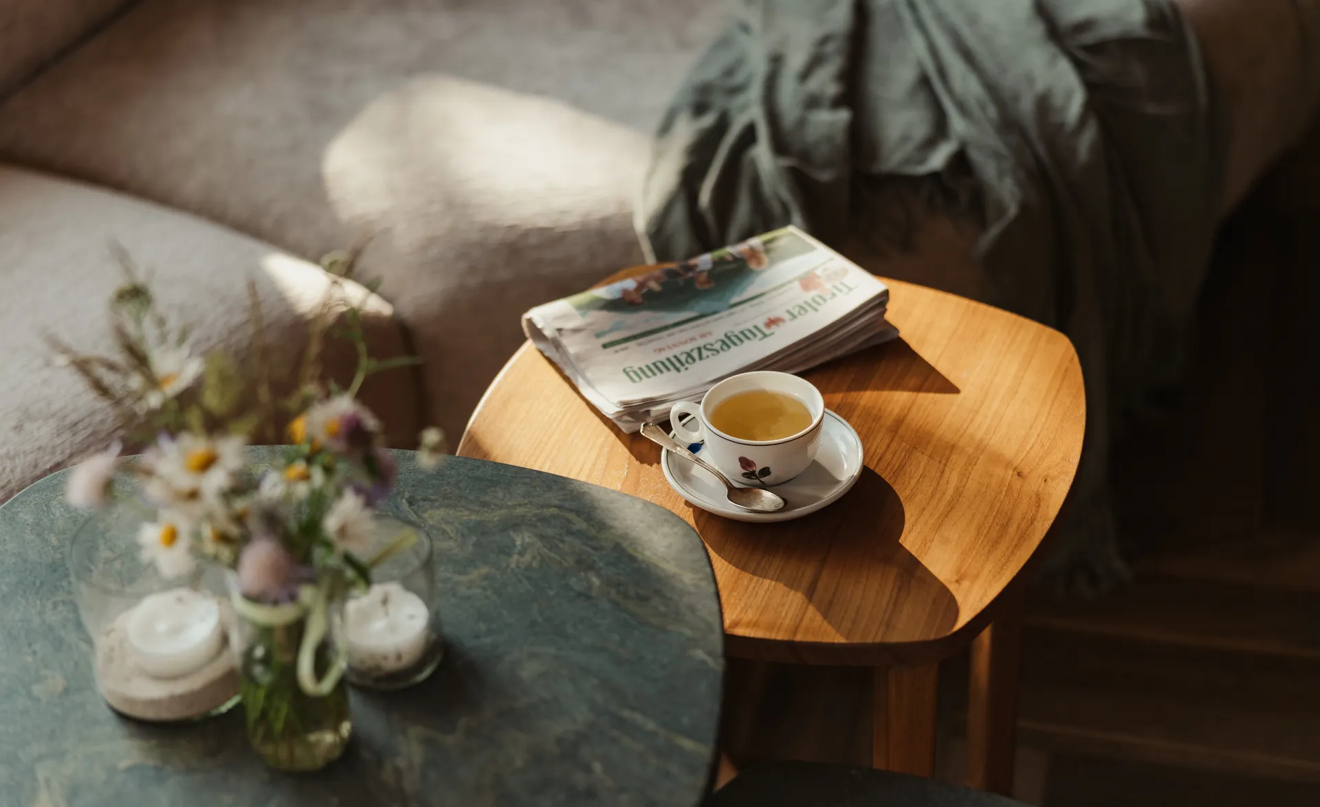 Teetasse und Zeitung auf Holz-Beistelltisch mit Wildblumen, Kerzen und Decke