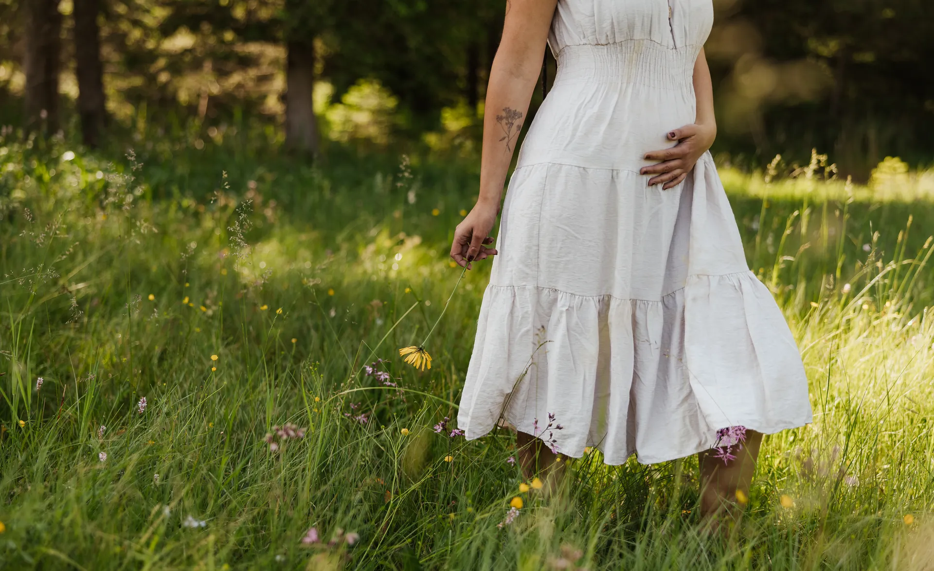 Frau im Leinenkleid steht in Wildblumenwiese am Waldrand in Stille und Ruhe
