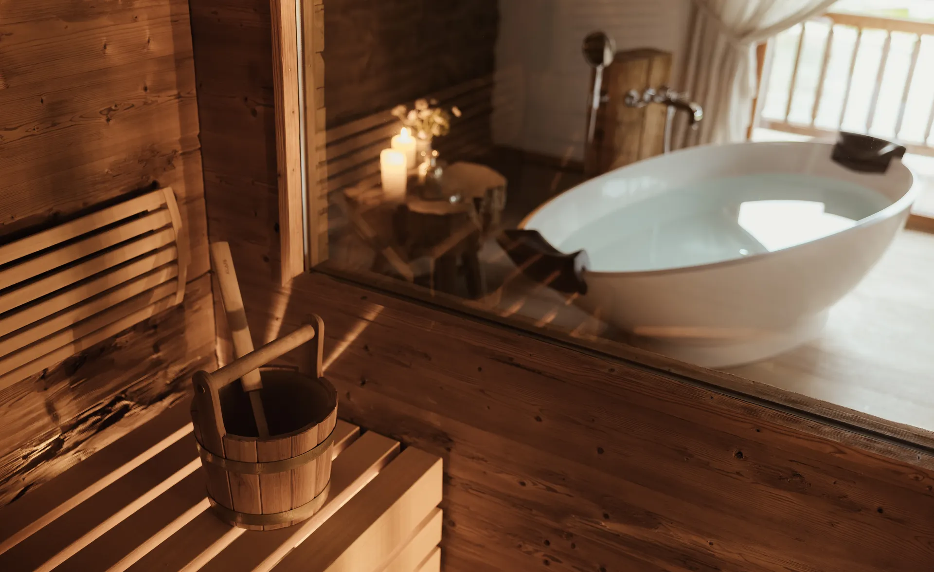 Chalet-Spa mit Holzsauna, Wassereimer und freistehendem weißem Badebottich bei Kerzenschein