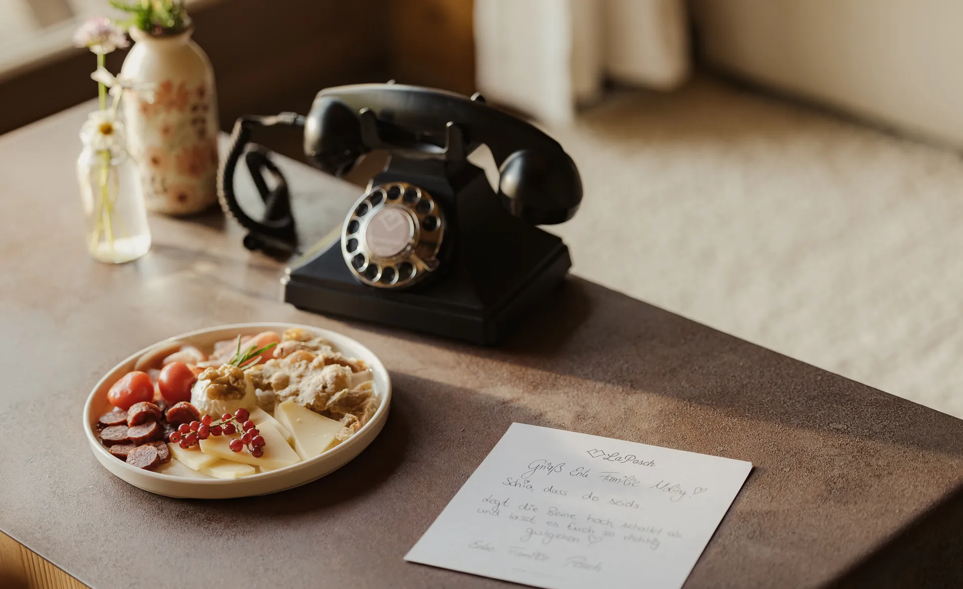 Willkommens-Stilleben im Chalet: Vintagetelefon, handgeschriebene Note und Käse-Charcuterie-Teller