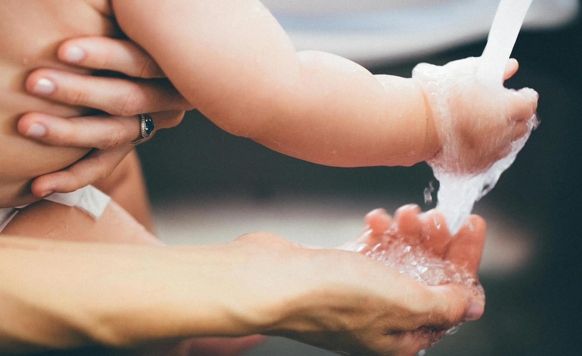 Einfühlsame Hände waschen Babyhand unter fließendem Wasser im sanften Licht