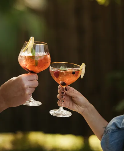 Zwei Frauen stoßen lachend mit eleganten Cocktailgläsern im Freien an