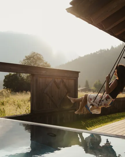 Woman swinging on a wooden swing beside the infinity pool with Zugspitze views