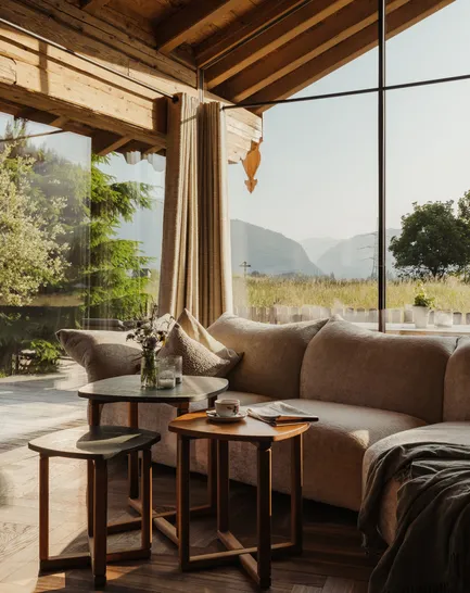 Chalet living room with glass facade, corner sofa, wooden beams and meadow and peak views