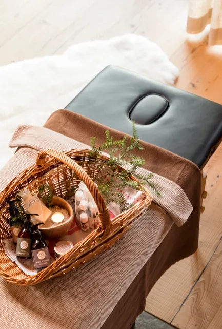 Massageliege mit natürlichen Spa-Produkten, Ölen, Kerze und Fichtenzweig-Korb