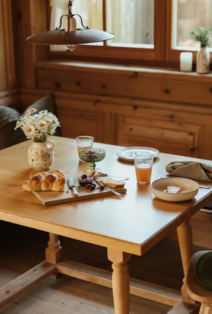 Gemütliche Zirbenholz-Frühstücksnische mit gedecktem Tisch, Saft und Gänseblümchen