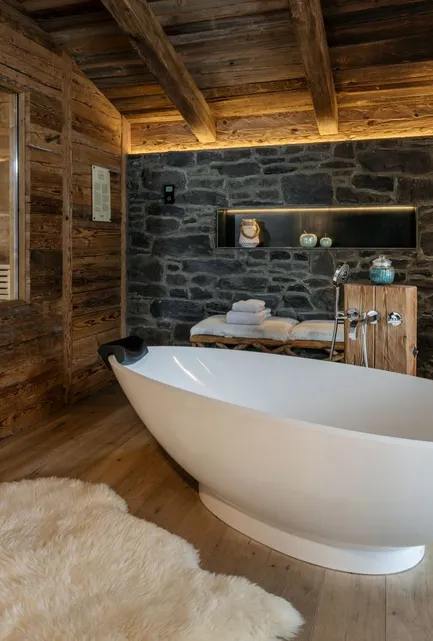 Luxuriöses Spa-Badezimmer mit freistehendem Badebottich, dunkler Steinwand und Glasfront-Sauna