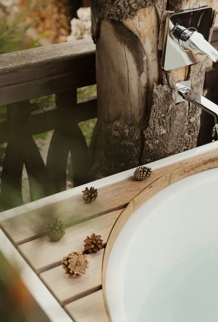 Wasserstrahl füllt Outdoor-Badebottich am Baumstamm-Armatur mit Fichtenzapfen-Dekor