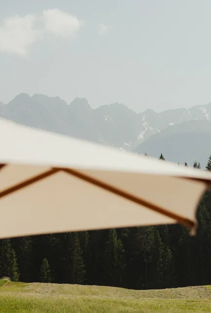 Creme-Sonnenschirm auf Terrasse vor unscharfer Kulisse aus Bergkuppen und Waldrand