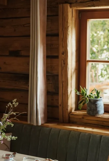 Chalet-Essecke mit dunkel geräuchertem Holz, grüner Sitzbank, Wildblumen und rustikalem Geschirr