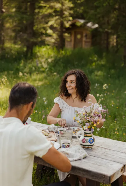 Lachendes Paar beim romantischen Abendessen am rustikalen Holztisch in der Almwiese