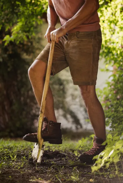 Mann in Lederhosen gräbt mit Holzspaten im Gartenbereich des LaPosch Resorts