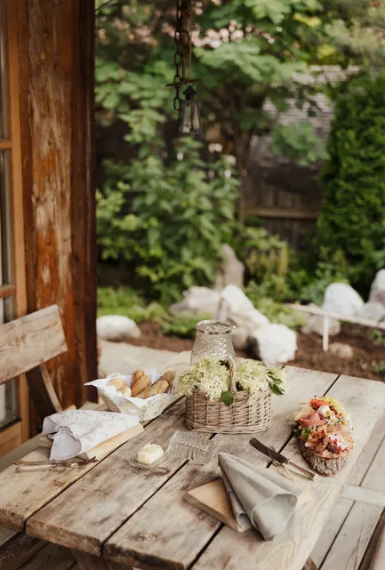 Rustikaler Holztisch im Garten mit Brotkorb, Holunderblüten und Leinenservietten