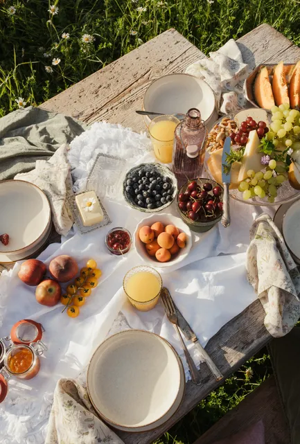 Prachtvoll gestalteter Frühstückstisch in blühender Wiese mit Keramik und Obst