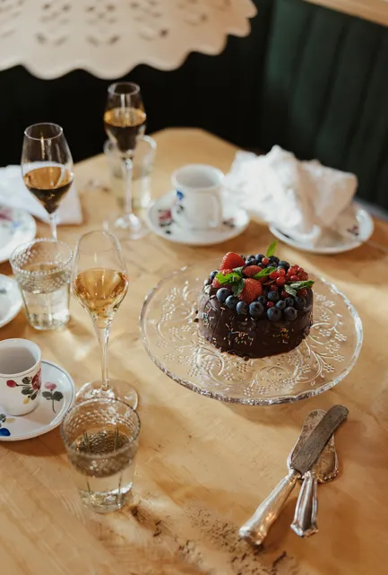 Aufsicht auf Beerentorte unter Glasglocke mit Sekt, Floraltassen und Kuchenbesteck