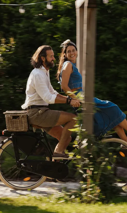 Lachendes Paar fährt auf Vintage-Fahrrad durch den sommerlichen Garten des LaPosch Resorts