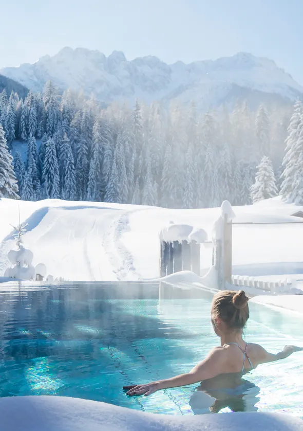 Frau entspannt im Außen-Infinity-Pool des LaPosch Chalets mit Winterbergpanorama