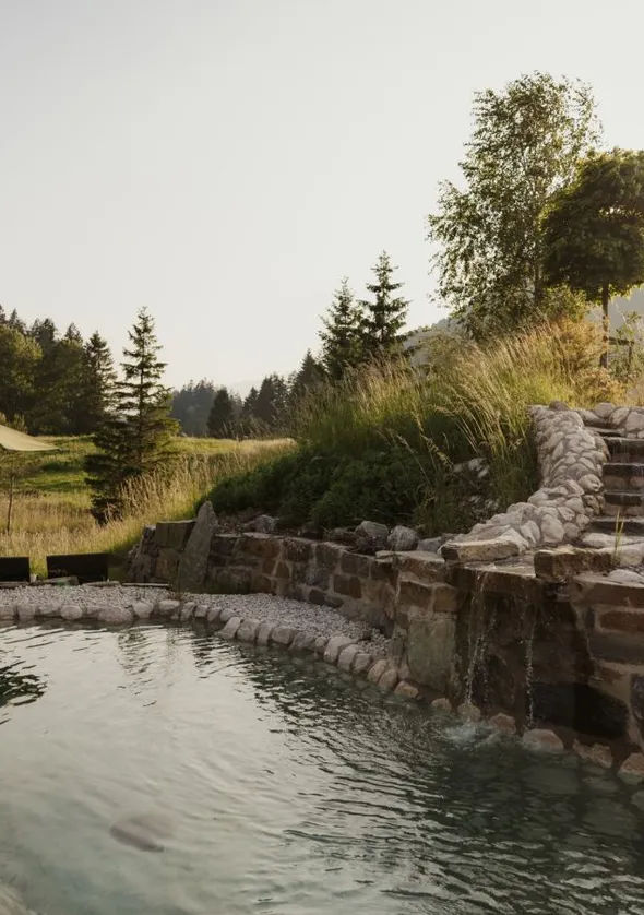 Natursteinpool mit Wasserfall und Kaskaden-Rinne in sommerlichem Tiroler Abendsonnenlicht