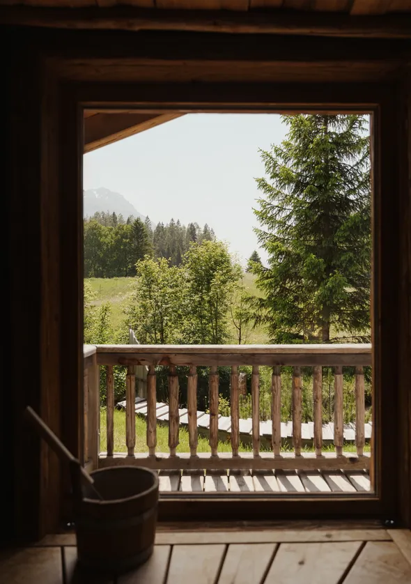 Chalet-Balkon mit Holzgeländer, Fichtenblick und Saunaeimerdetail auf Fensterbrett