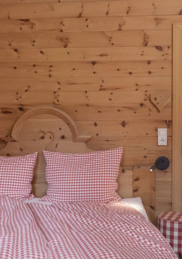 Zirbenholz-Schlafzimmer mit Schnitzholzbett, karierter Bettwäsche und Blick in Sauna