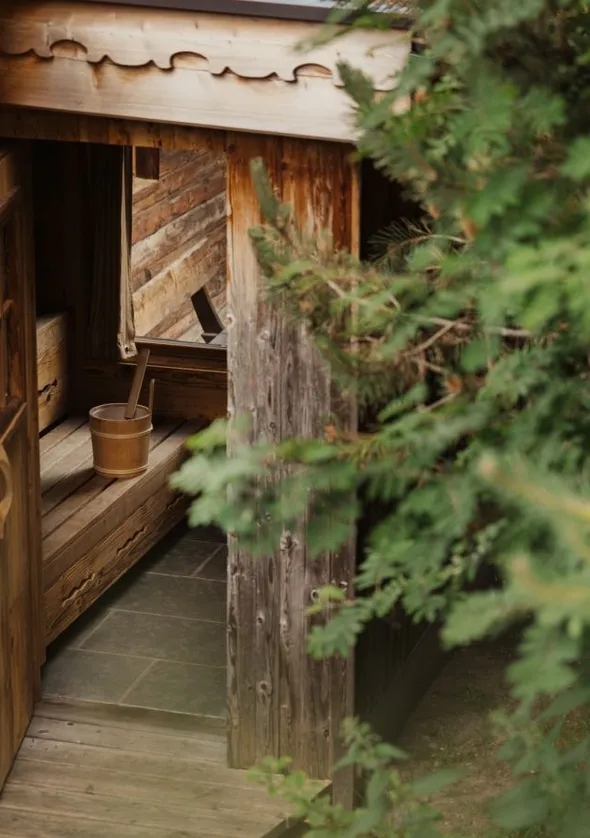 Rustikale Außensauna-Hütte mit Holzschnitz-Tür, Eimer und Naturstein-Boden im Bergwald