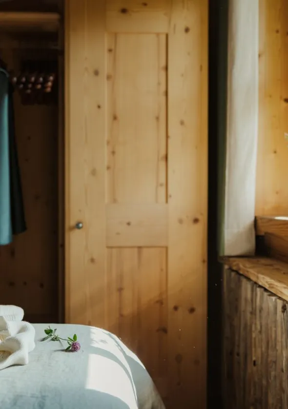 Soft-beleuchtete Chalet-Schlafzimmerecke mit Zirbenholz, Bademantel und Wildblume auf Bettlaken