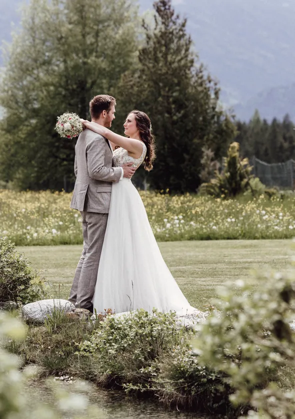 Brautpaar umarmt sich im grünen Chalet-Garten mit Wildblumen und Tiroler Bergkulisse