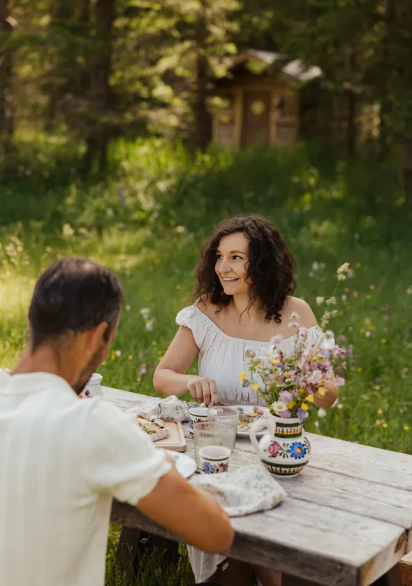 Lachendes Paar beim romantischen Abendessen am rustikalen Holztisch in der Almwiese