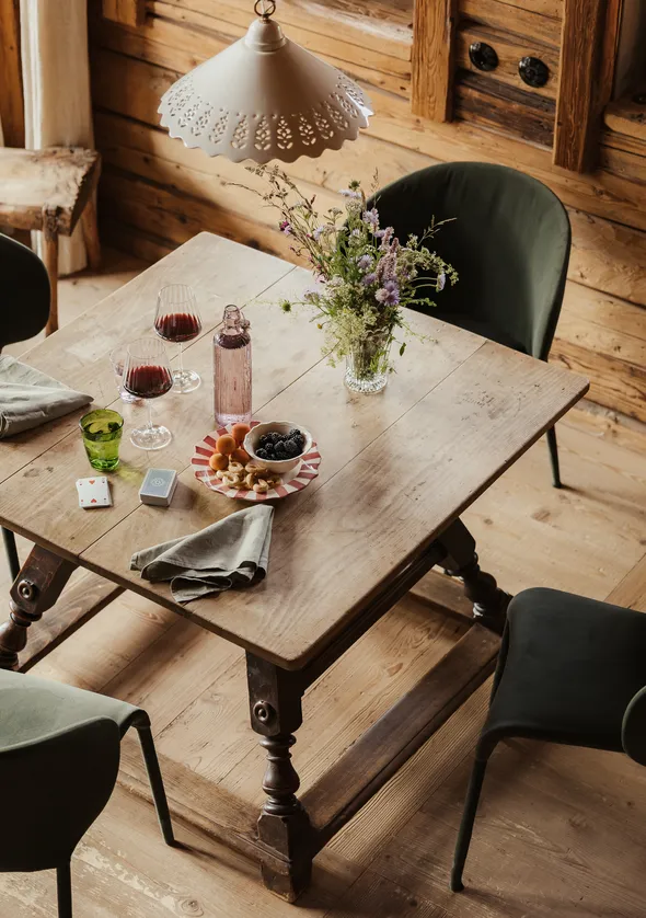 Rustikale Chalet-Essecke von oben mit Holztisch, Wildblumen und grünen Samtstühlen