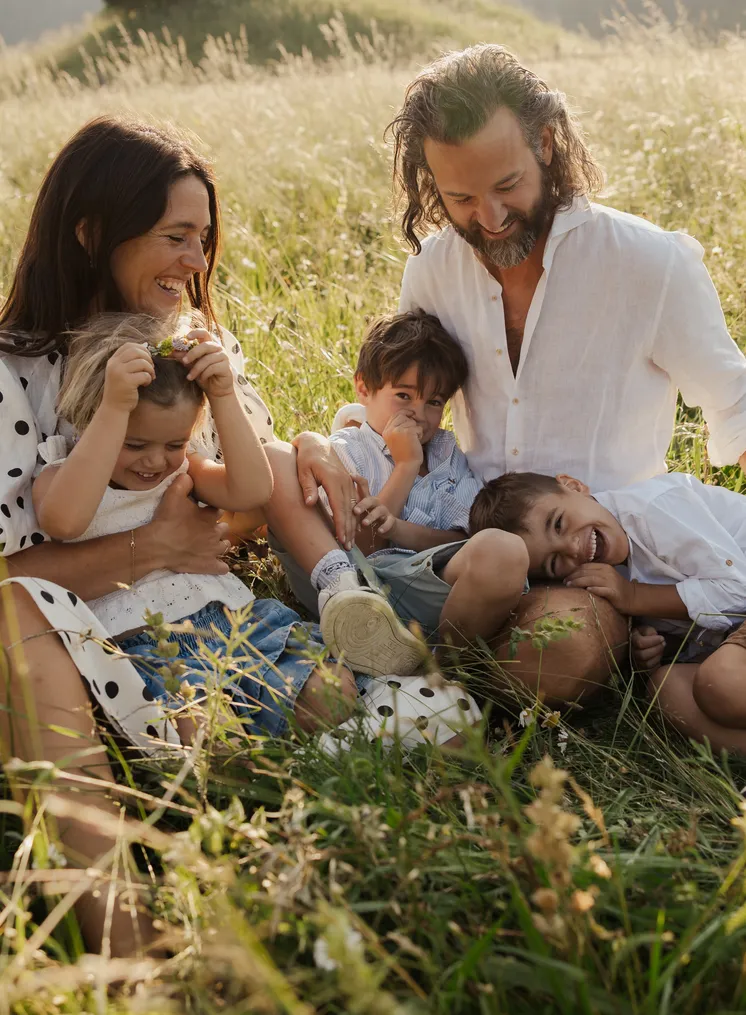 Fünfköpfige Familie lacht und kuschelt glücklich im hohen Sommergras