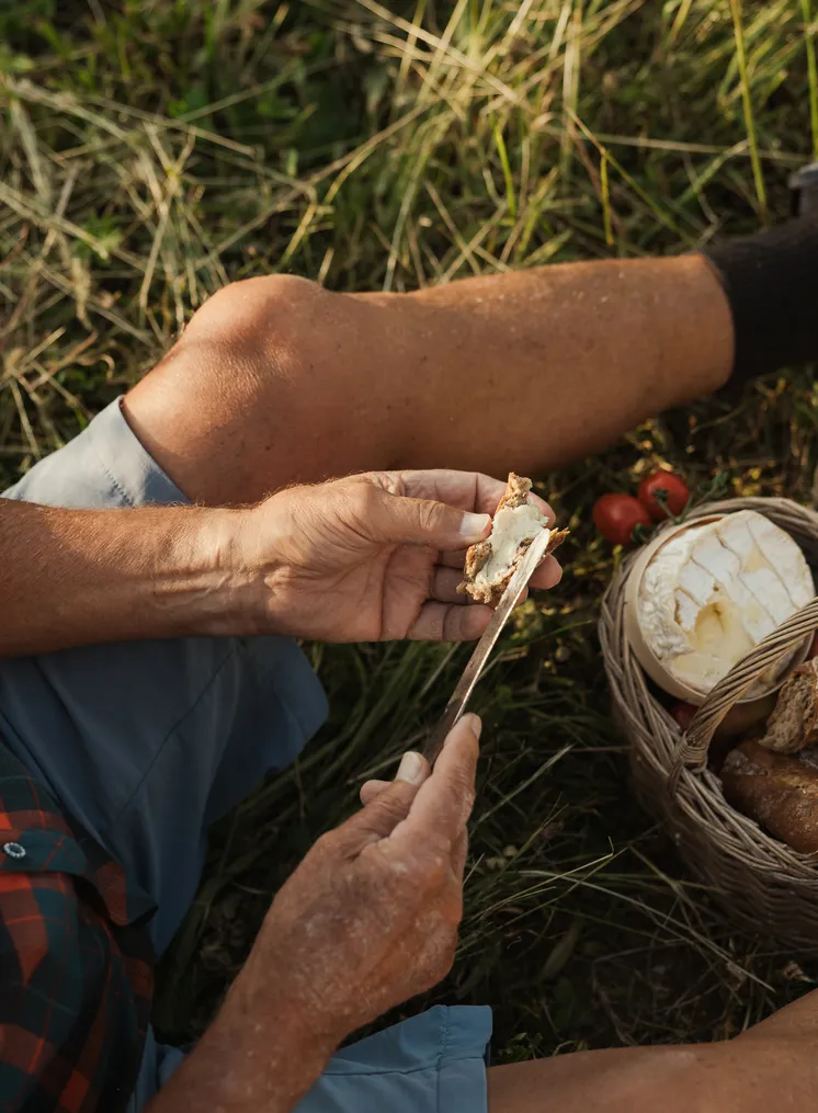 Älteres Paar picknickt im Gras und bereitet gemeinsam Brot und Käse vor