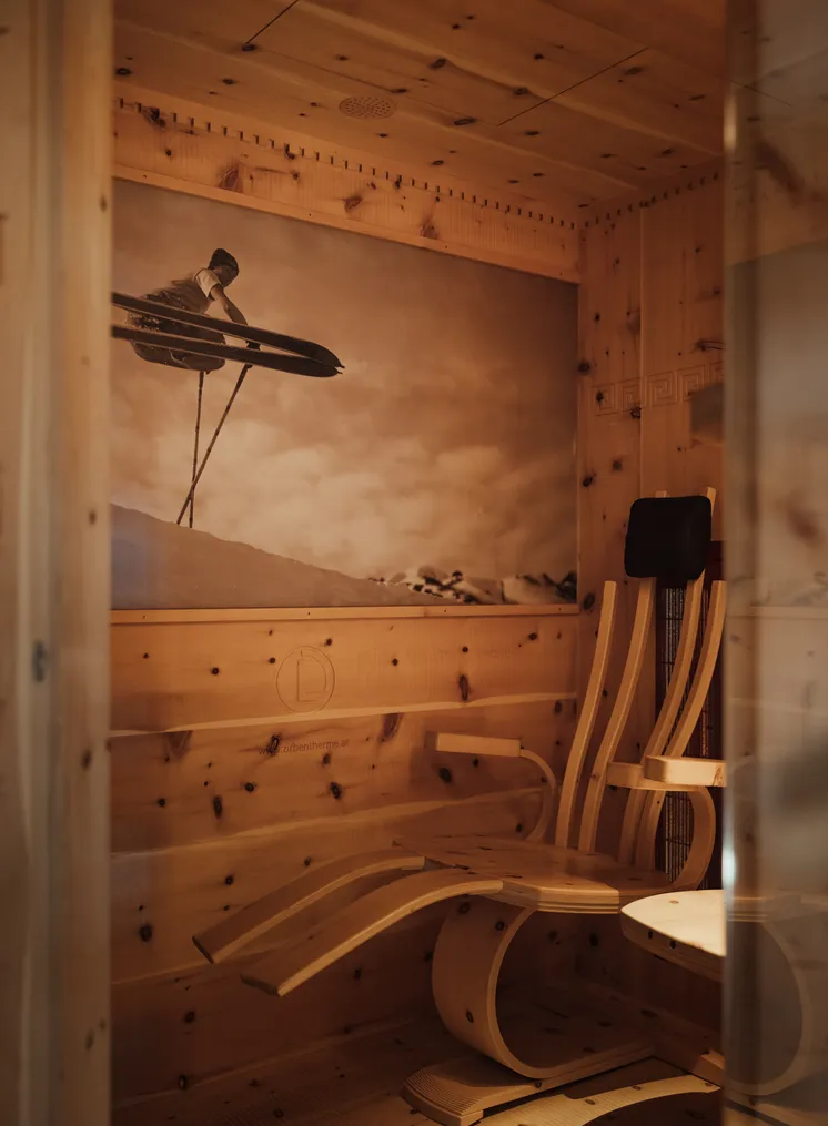 Kleines Zirbenholz-Saunainnere mit geschwungenem Holzlieger und Vintage-Ski-Foto