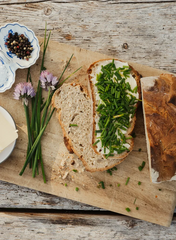 Flatlay von frischem Bauernbrot mit Butter und Schnittlauch auf Holzunterlage