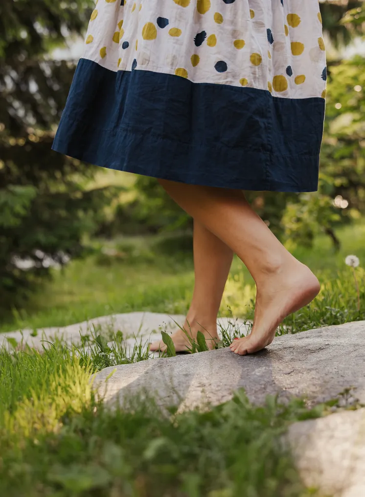 Nackte Frauenbeine in gepunkteter Leinenkleid auf Naturstein zwischen Grasfläche