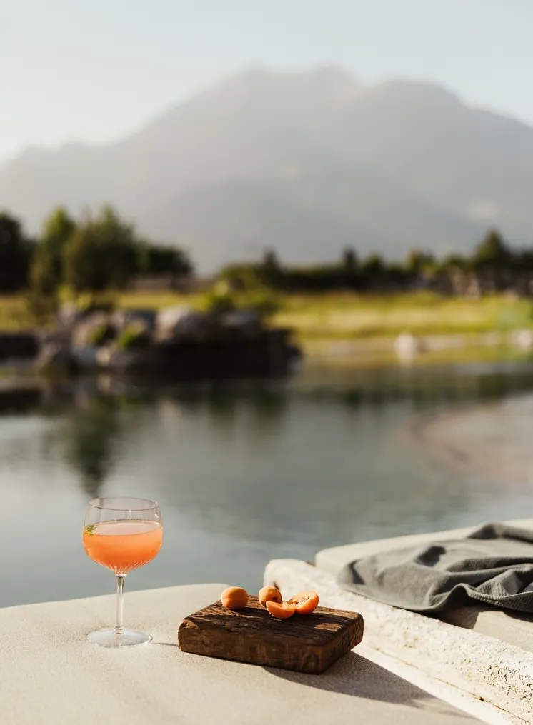 Pfirsich-Aperitif im Stielglas mit Marillen auf Holzbrettchen am Natursee