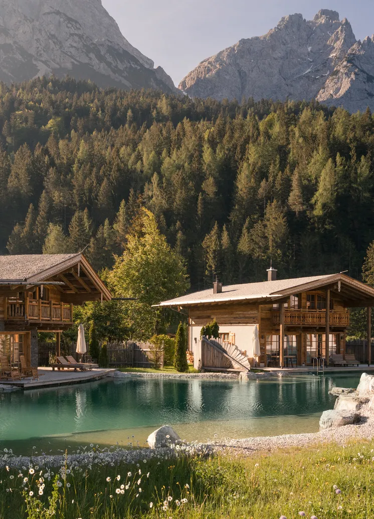 LaPosch Holzchalets am Naturbadesee mit dramatischer Felswand und Wald im Hintergrund